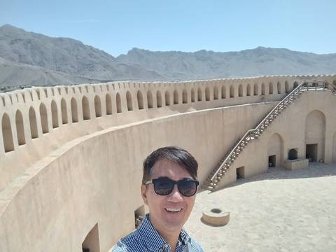       A person wearing sunglasses standing in a fort with arched walls and mountains in the background.
  