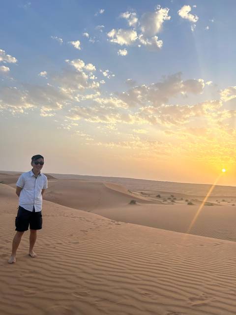       A person standing in a desert during sunset with clear skies and sand dunes.
  