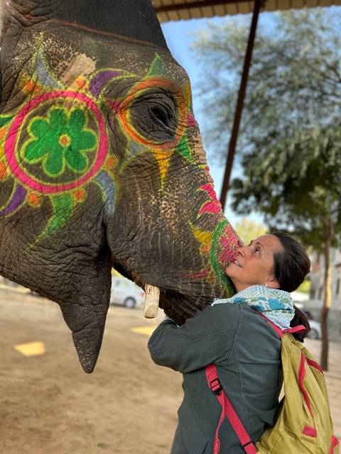 A woman interacting with a colorfully painted elephant.