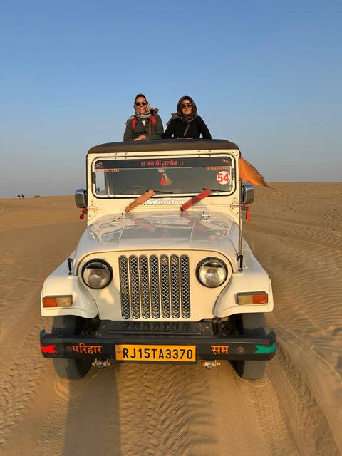 A decorated jeep parked in the desert with a camel in the background.
