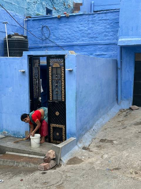       A woman in a sari posing at the doorway of a blue building.
  