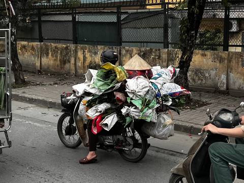       Motorcycle overloaded with bags and a person wearing a conical hat.
  