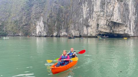       People kayaking in a calm body of water with rocky cliffs.
  