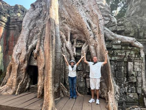       Tourists posing under a giant tree entwined with ancient ruins.
  