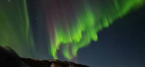       Northern lights illuminating the night sky with mountains below.
  