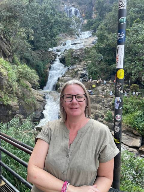Woman posing in front of a waterfall with people in the distance.