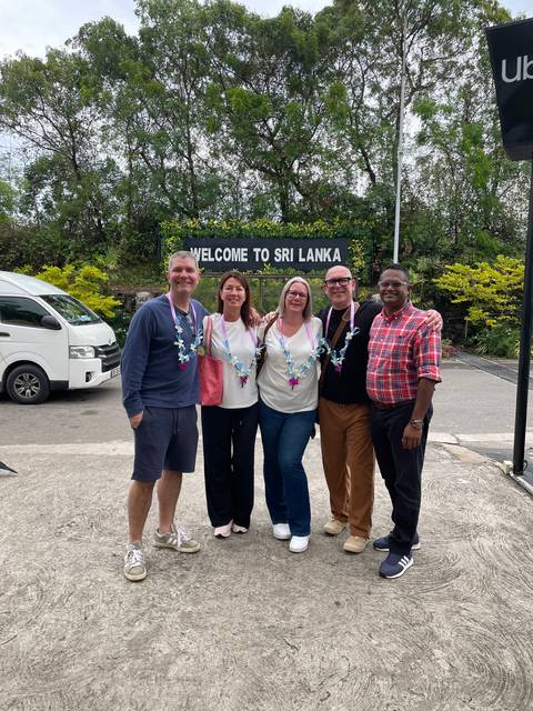 Five tourists in front of a sign welcoming them to Sri Lanka.