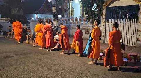 Monks in orange robes walking in a line on a street at night.