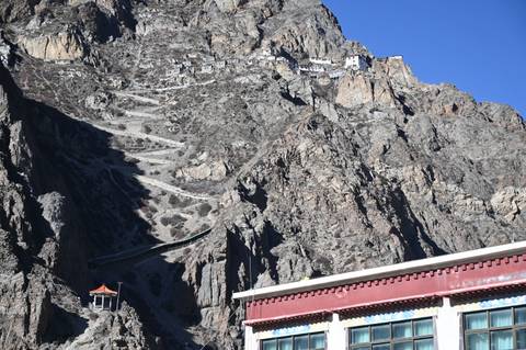 Steep mountain path with small buildings on rugged cliffs.
