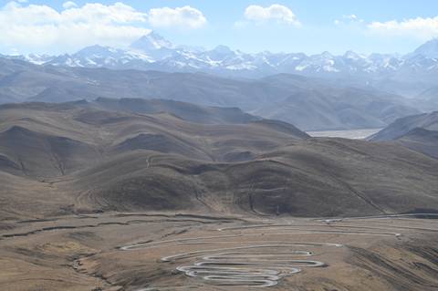 Mountains with winding road paths and snow-covered peaks in the distance.