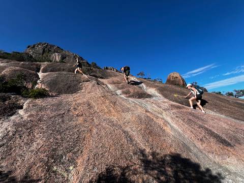 People hiking on a rocky mountain path under clear blue skies.