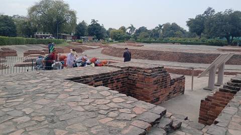 A group of tourists gathered around ancient brick ruins in a park setting.