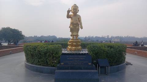 Golden statue surrounded by garden with people in the background.