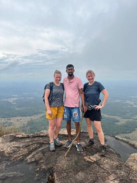 Three people posing on a hilltop with a view of the terrain below.