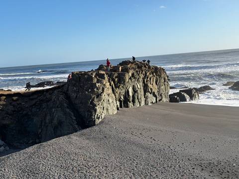      Rocky coastline with waves breaking against it and people on top.
  