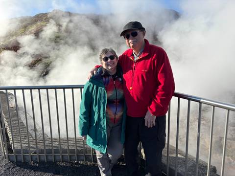       A couple standing in front of a steaming geothermal area.
  