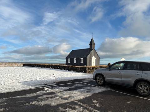       A small black church with a car parked in the snowy landscape.
  