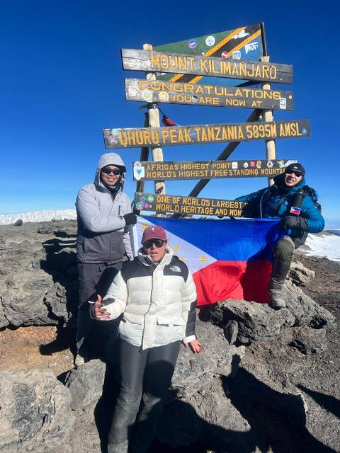 Group of three people at Uhuru Peak with a flag and sign.