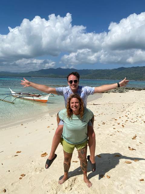 Couple posing on a tropical beach with clear water and traditional boat.