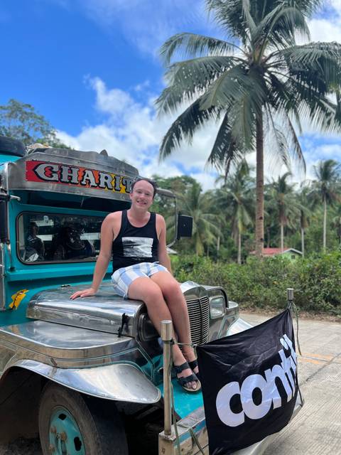 Person sitting on a decorated jeepney with palm trees in the background.