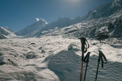 Snow-covered mountain landscape with two hiking poles in the foreground.
