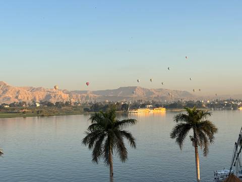 Hot air balloons over a river and mountains at sunrise.