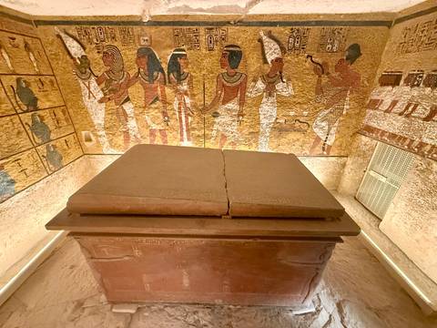       A stone sarcophagus in a tomb with wall paintings.
  