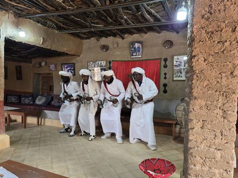 Group of men in traditional attire performing a dance indoors.