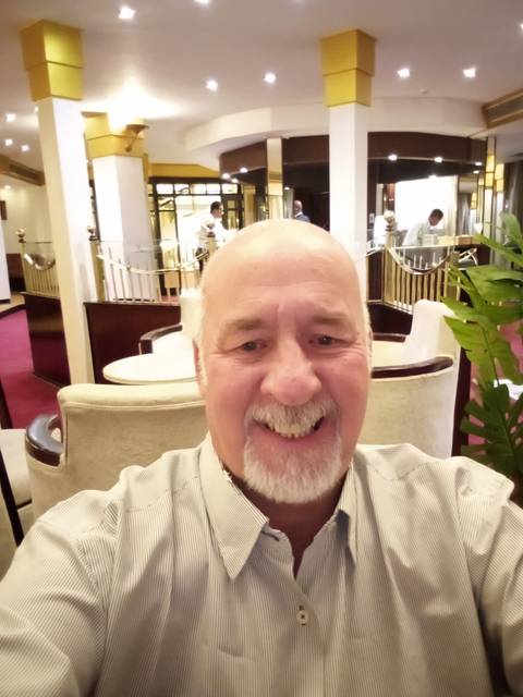 Selfie of a smiling man indoors with dining area in background.