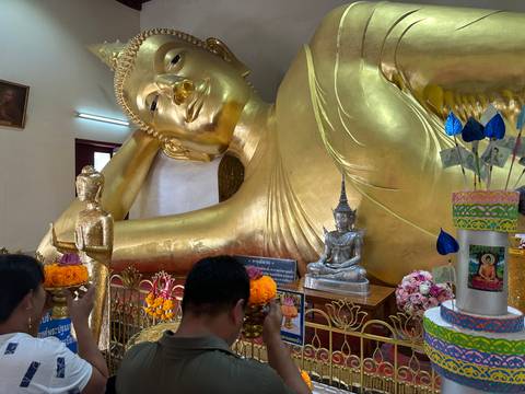       People praying in front of a reclining golden Buddha statue.
  