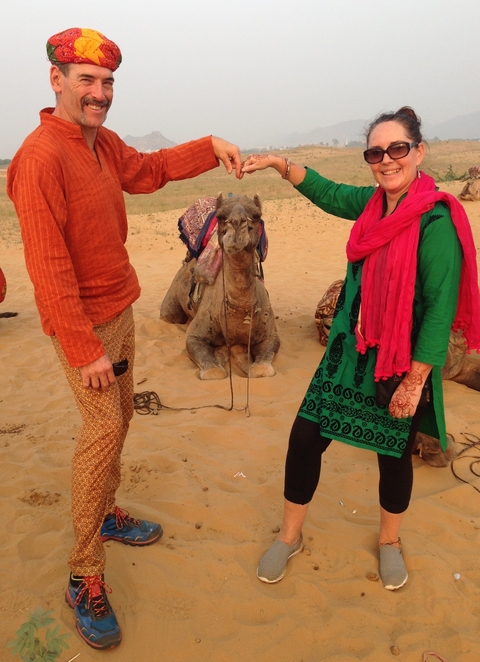 Two people with a camel on sandy terrain.
