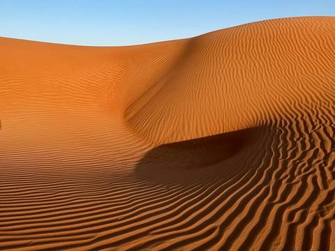Beautifully patterned sand dunes under clear sky.