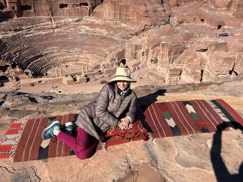       Woman reclining on a rug with ancient amphitheater in background.
  