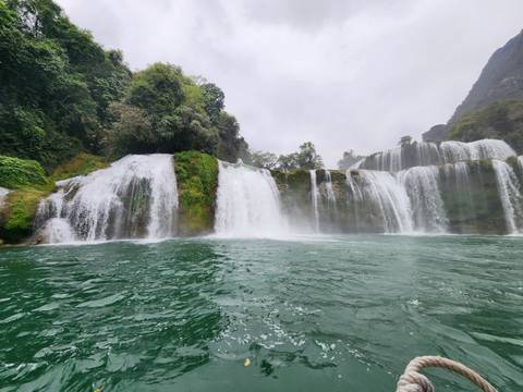       Waterfall flowing into a river with greenery around.
  
