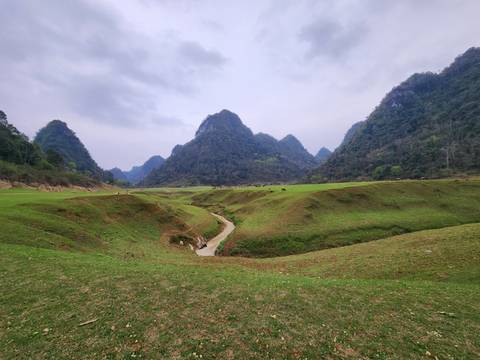       Expansive green valley with mountains under a cloudy sky.
  