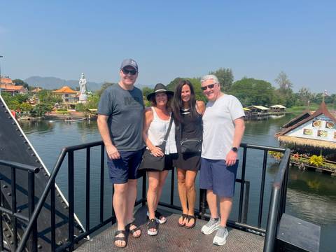 People posing on a bridge with water and trees in the background.