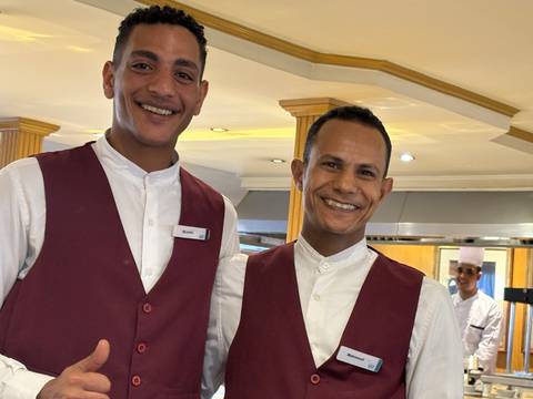 Two smiling men in uniforms standing in a restaurant setting.