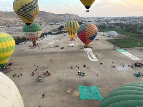       Aerial view of hot air balloons on a field with mountains in the background.
  