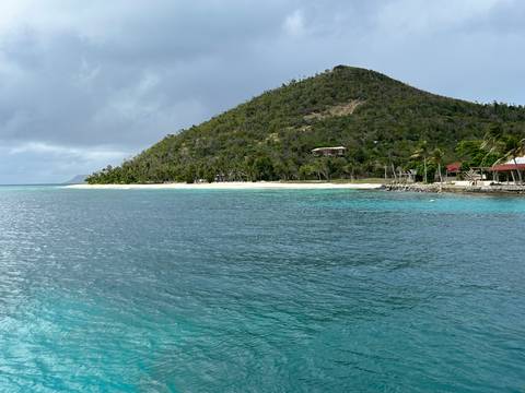 Beach with turquoise water and a hill in the background.