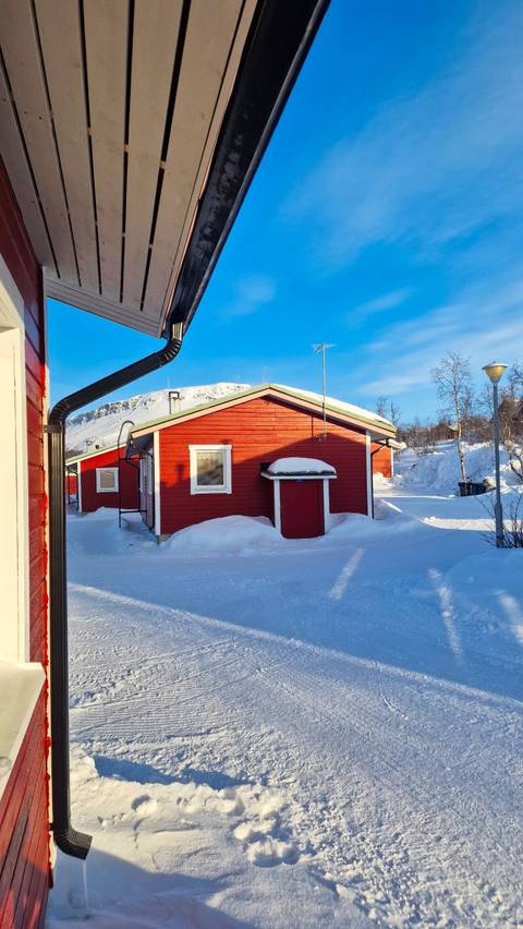 Red wooden cabin in a snowy landscape with a mountain backdrop.