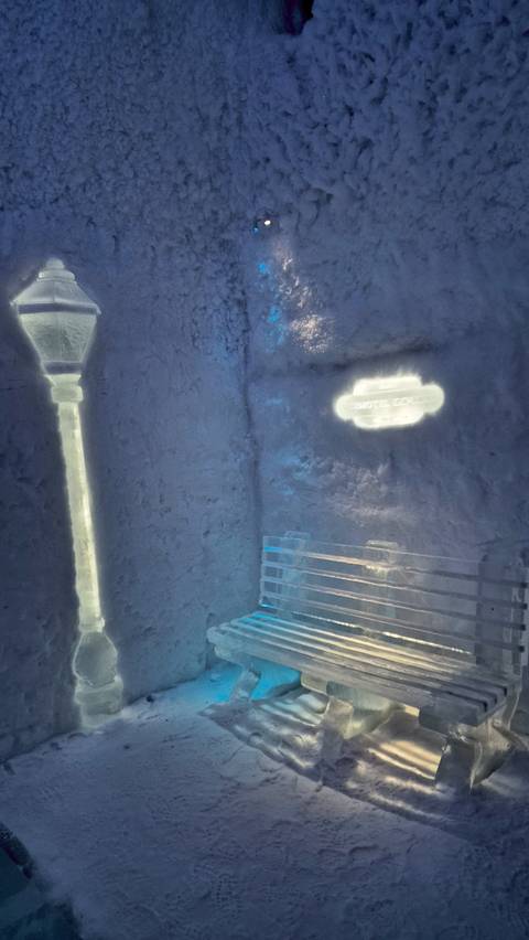Ice hotel interior with benches and glowing signs.