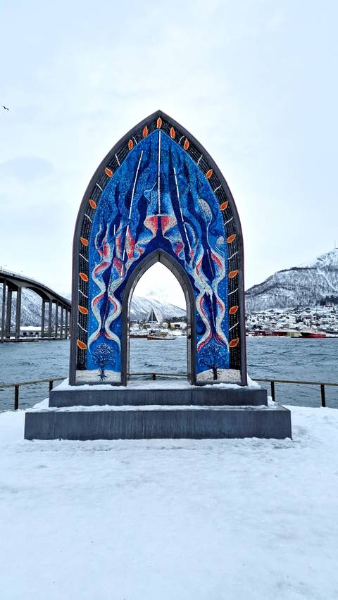 Artistic blue arch with view of Tromso bridge and water.
