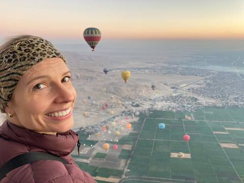 A person in a hot air balloon over a landscape with other balloons.