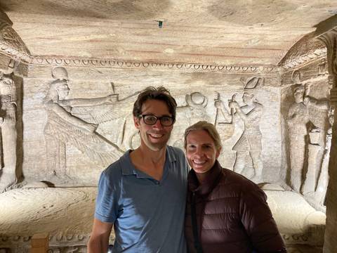 Two people posing inside a historic site with ancient carvings.
