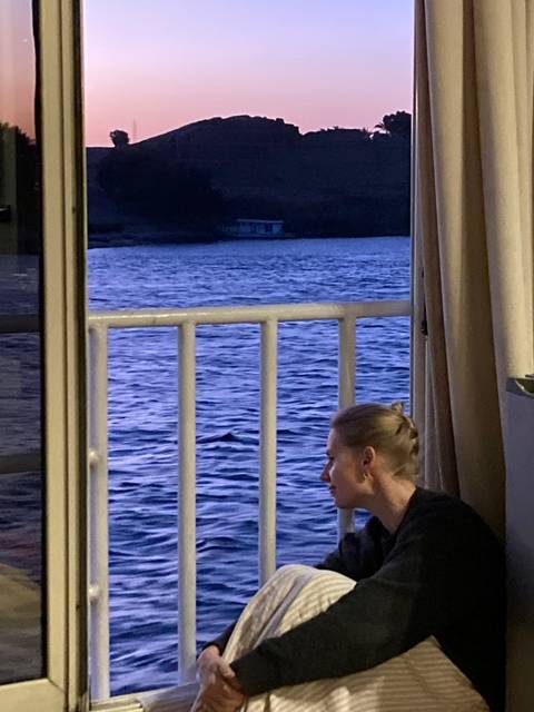 A person sits on a boat balcony with a river view.
