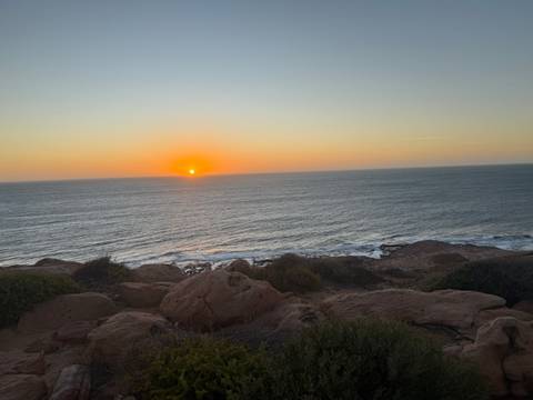Sunset over the ocean with a rocky coastline.