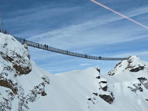 Suspension bridge over snowy mountains with people walking.
