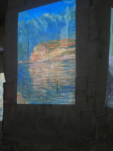 Projected image of a painting with water and mountains on a wall.