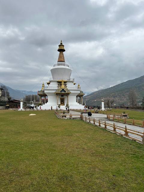 Large white stupa with golden decorations in a landscaped area.