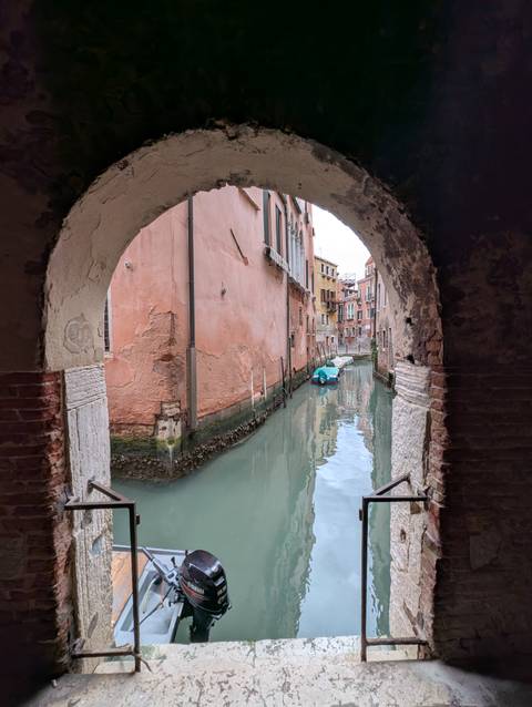       Venetian canal with a small boat visible through an archway.
  